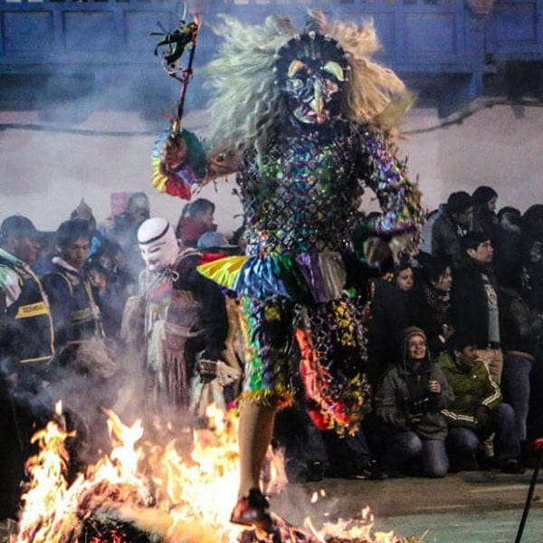 A person in costume standing on fire with people watching.