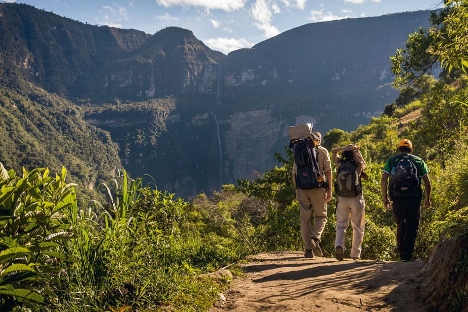 Two people walking on a trail in the mountains.