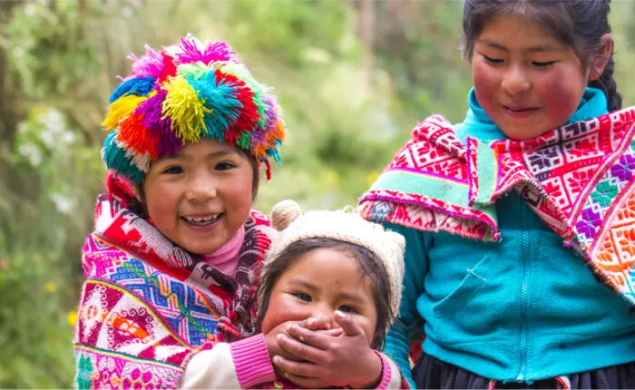 Three children in colorful clothing and hats are smiling.