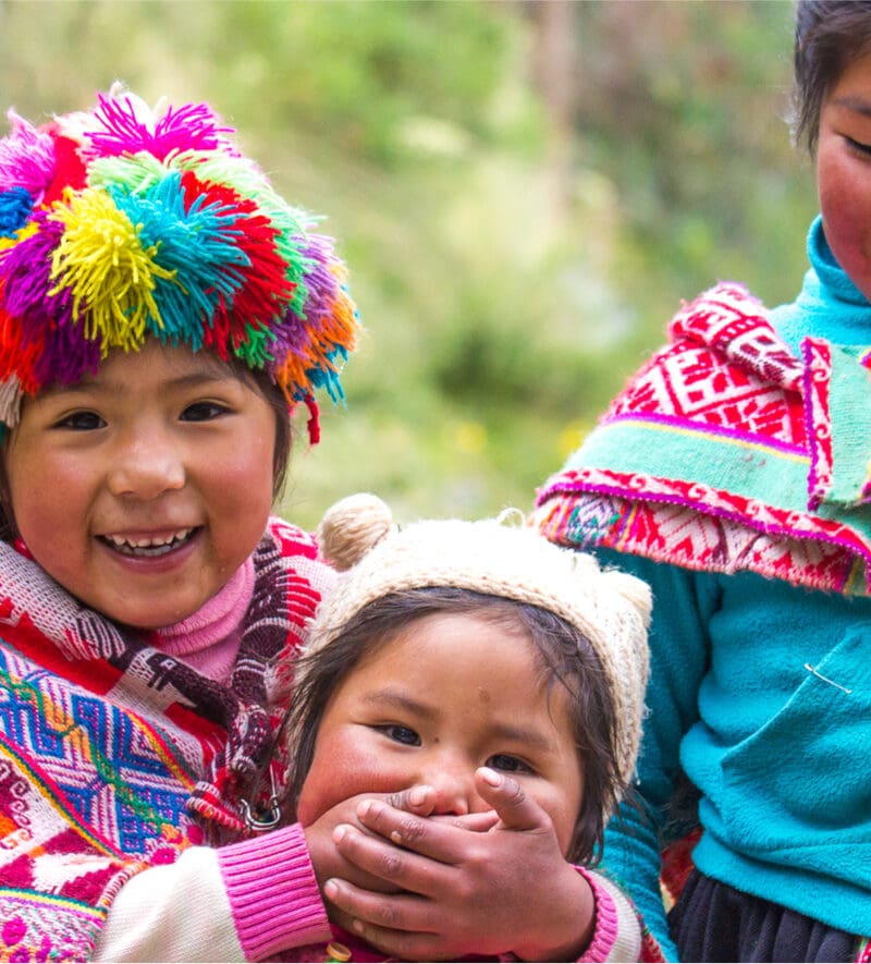 Three children in colorful clothing and hats are smiling.